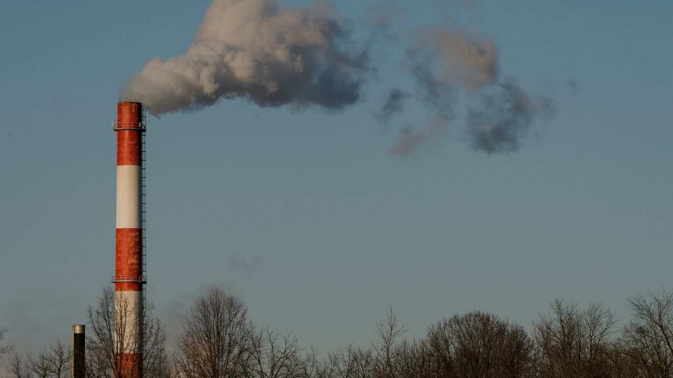 Smoke billows from a striped industrial chimney against blue sky.